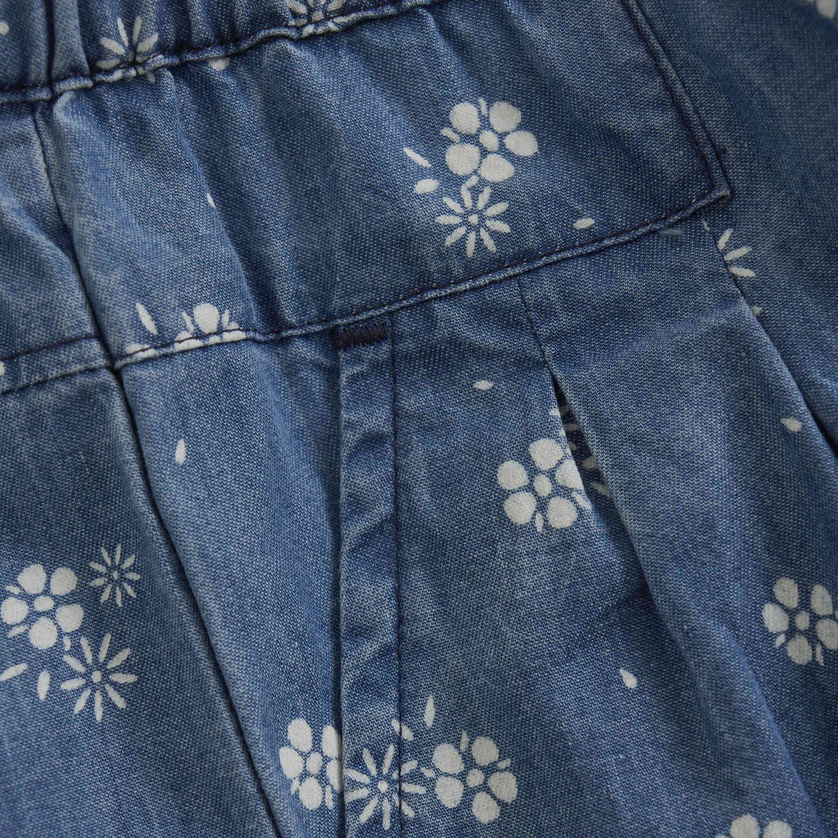 Eine Nahaufnahme eines blauen Stoffes mit weißen Blumenmustern. Der Stoff scheint Falten und Nähte zu haben, möglicherweise von einem Kleidungsstück wie einem Kleid oder Rock. Ideal für die Herstellung hochwertiger Kleidungsstücke wie GOTS-zertifizierter Kleider oder für diejenigen, die Minymo - Chambray-Hosen von Minymo mit einzigartigem Design kaufen möchten.