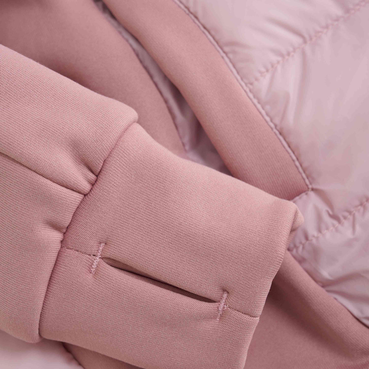 Nahaufnahme einer hellrosa Color Kids - Hybrid-Fleecejacke, die die Ärmel und einen Teil des Körpers zeigt. Der Stoff scheint eine Mischung aus weichem, gestepptem Material und einem glatten, sweatshirtähnlichen Material zu sein, mit sichtbaren Nähten und Nahtdetails, die den GOTS-Standards entsprechen.
