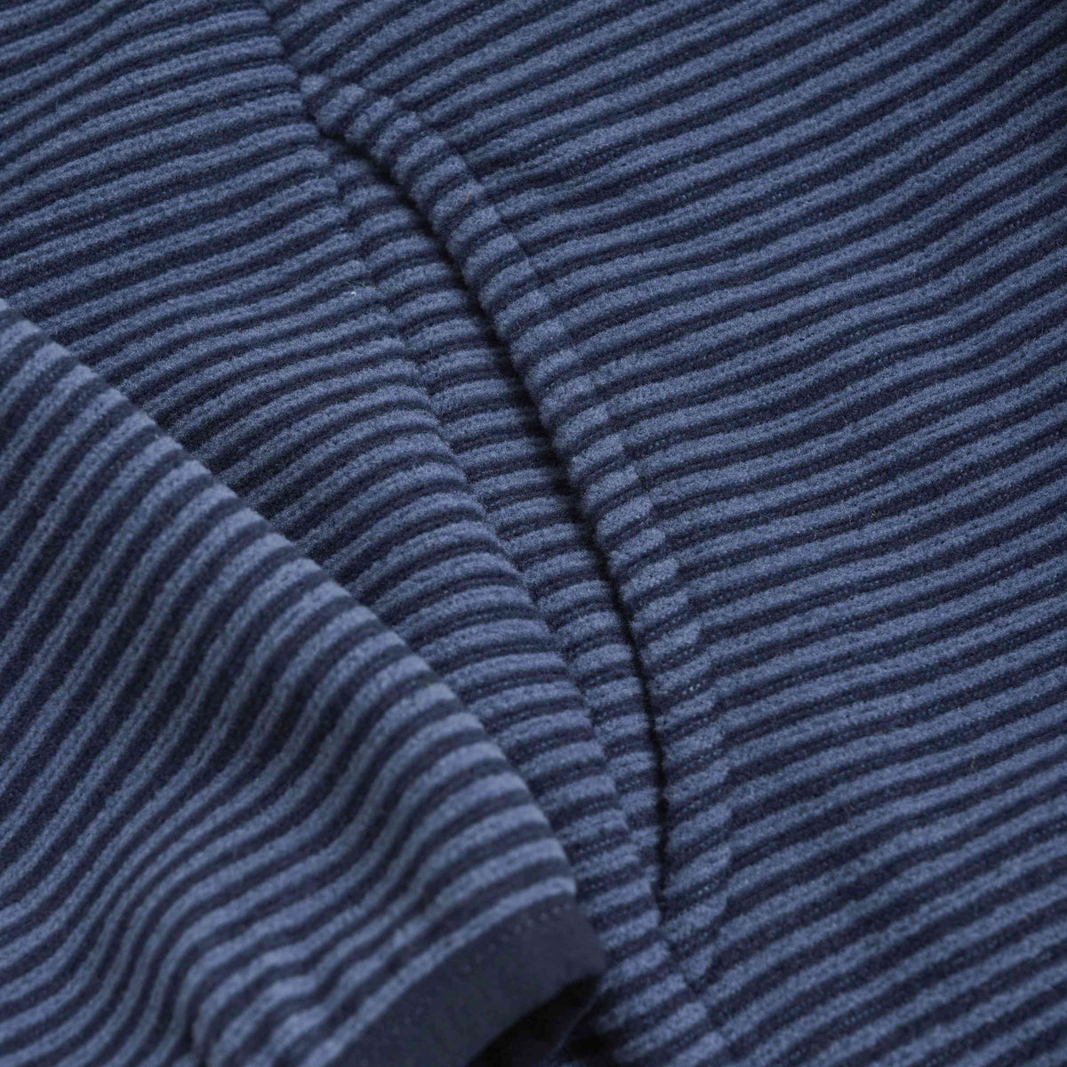 Nahaufnahme eines Kleidungsstücks mit einer Textur aus horizontalen blauen und schwarzen Streifen. Der Stoff wirkt weich und hat sichtbare Stiche, die auf eine Naht hinweisen. Die gleichmäßig gemusterten Streifen geben einen detaillierten Blick auf das Material frei, ideal für eine Color Kids - Fleecejacke von Color Kids.