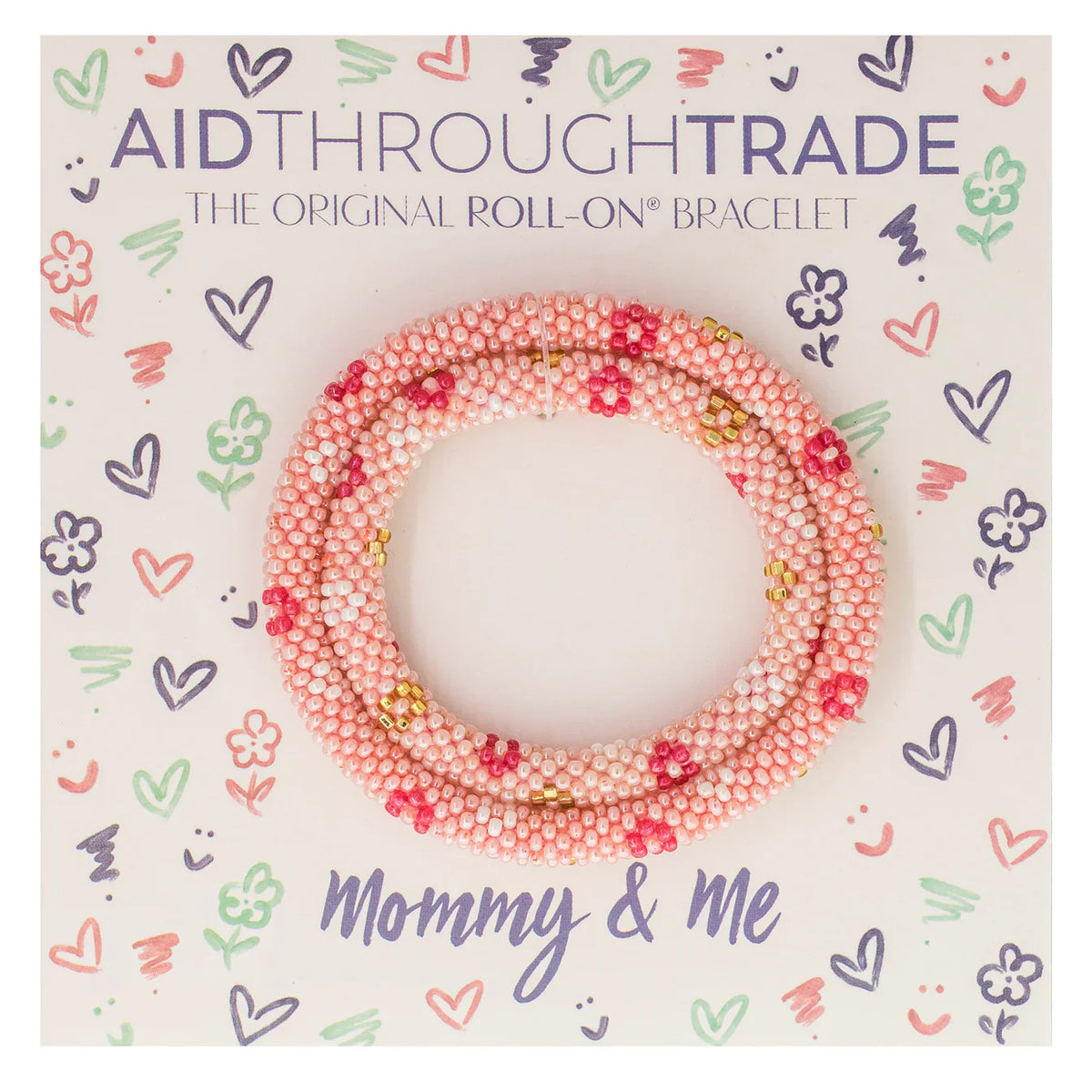 Ein verpacktes Set von Aid Through Trade - Armbänder Mommy & Me Roll-On® Armbändern, mit rosa und weißen Perlen mit Akzenten in Rot und Gold, hergestellt aus hochwertigen Glasperlen. Die verspielte Verpackung enthält Kritzeleien von Herzen, Blumen und Sternen mit dem Text „Aid Through Trade - Das Original Roll-On® Armband - Mommy & Me“.