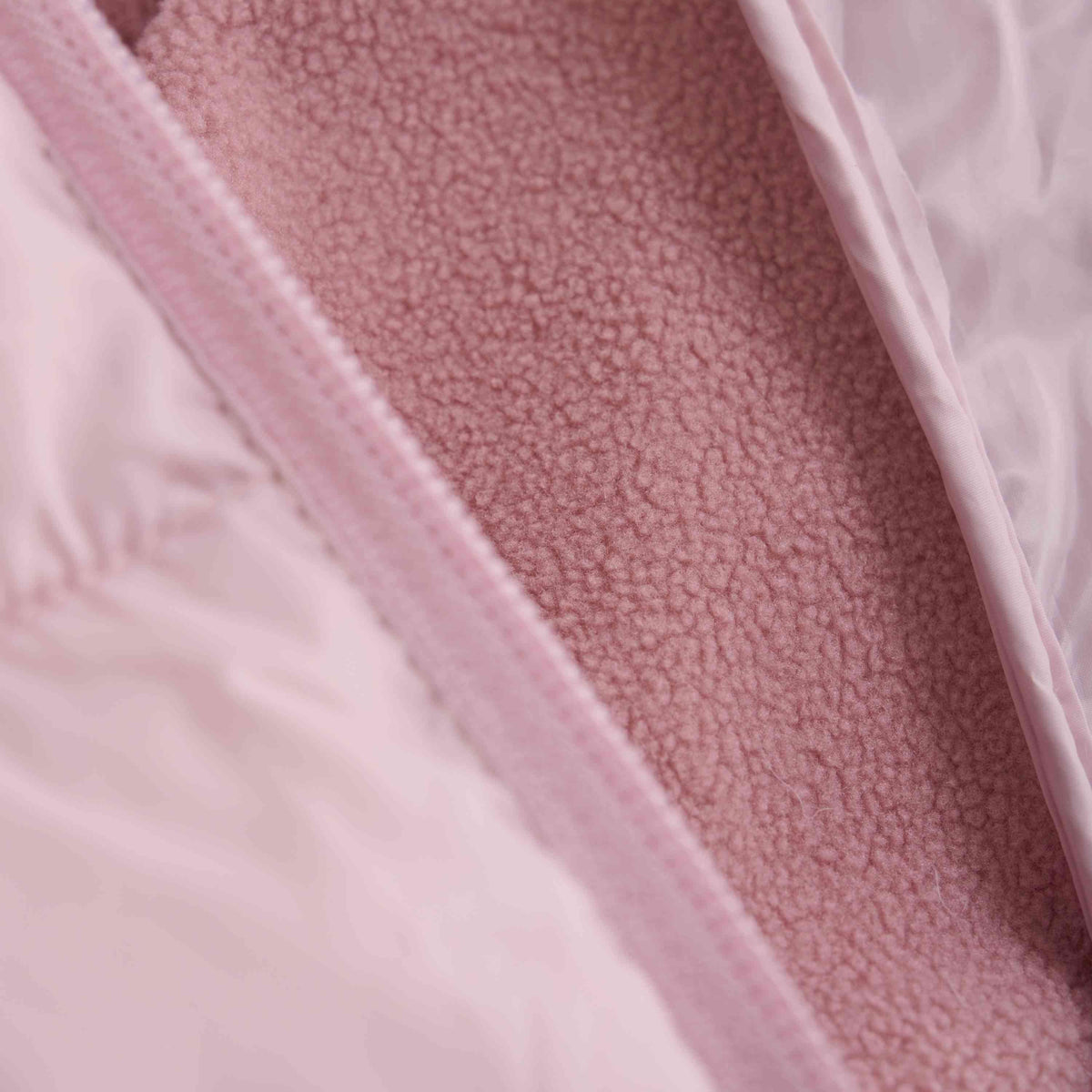 Nahaufnahme einer Color Kids - Hybrid-Fleecejacke mit teilweise geöffnetem Reißverschluss. Die linke Seite zeigt die glänzende Stoffaußenseite, während die rechte Seite das flauschige, strukturierte Innenfutter zeigt. Die kontrastierenden Materialien unterstreichen das Design und die Funktionalität der Jacke für Wärme und Komfort in den Übergangszeiten.